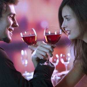 Young couple sharing a glass of red wine in restaurant, celebrating or on romantic date